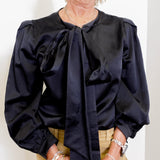 Person wearing a black blouse with a tie neckline against a white background
