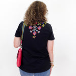 Person wearing a black t-shirt with colorful floral design on the back, standing against a white background.
