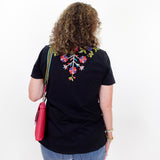 Person wearing a black t-shirt with colorful floral design on the back, standing against a white background.