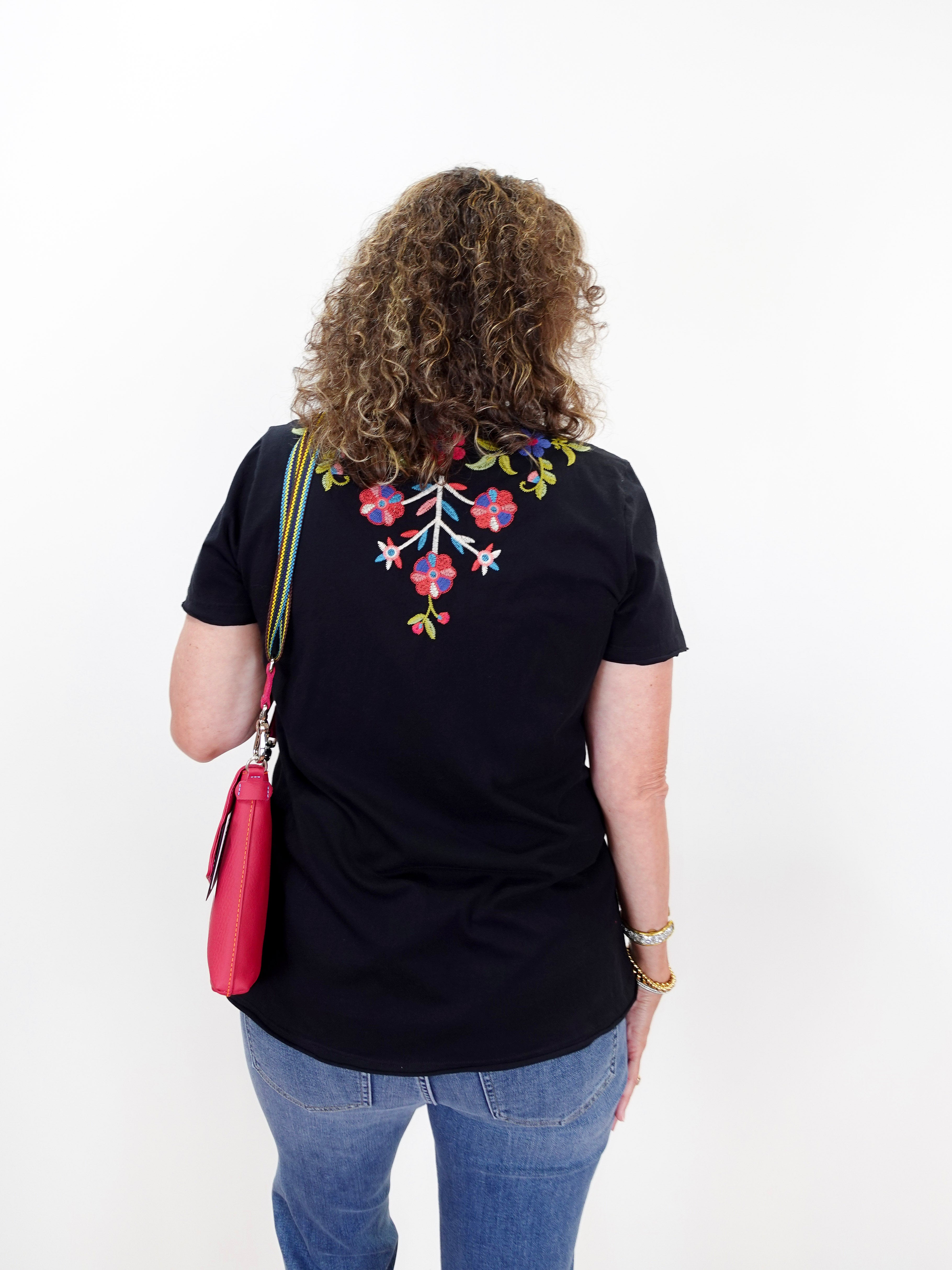Person wearing a black t-shirt with colorful floral design on the back, standing against a white background.