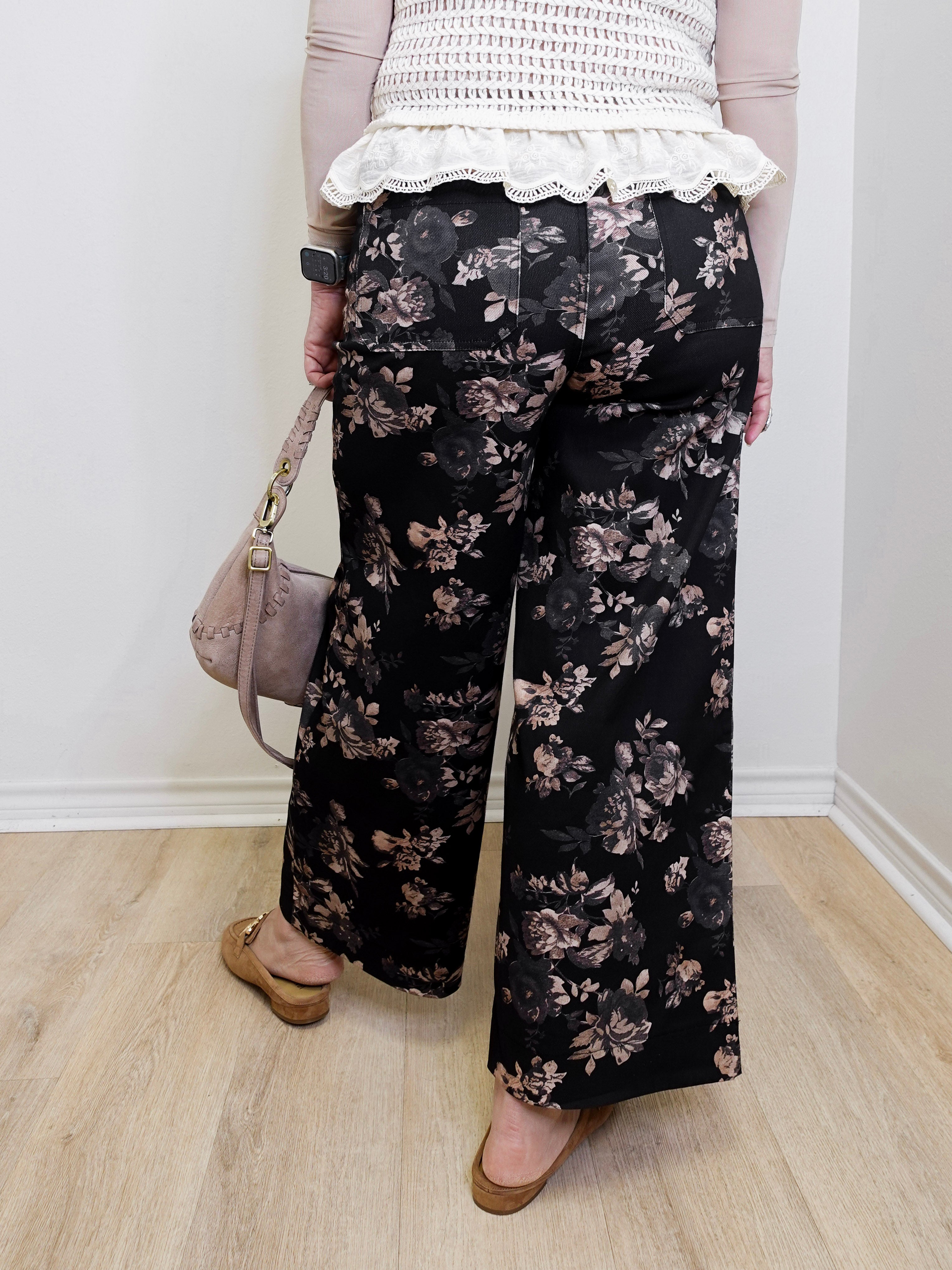 Person wearing black floral pants with a white lace top, standing indoors.