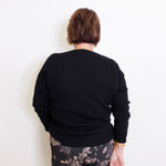 Person wearing a black sweater and patterned pants against a white background