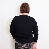 Person wearing a black sweater and patterned pants against a white background