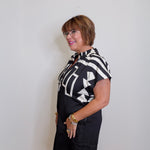 Woman wearing a black and white patterned blouse and black shorts against a plain background