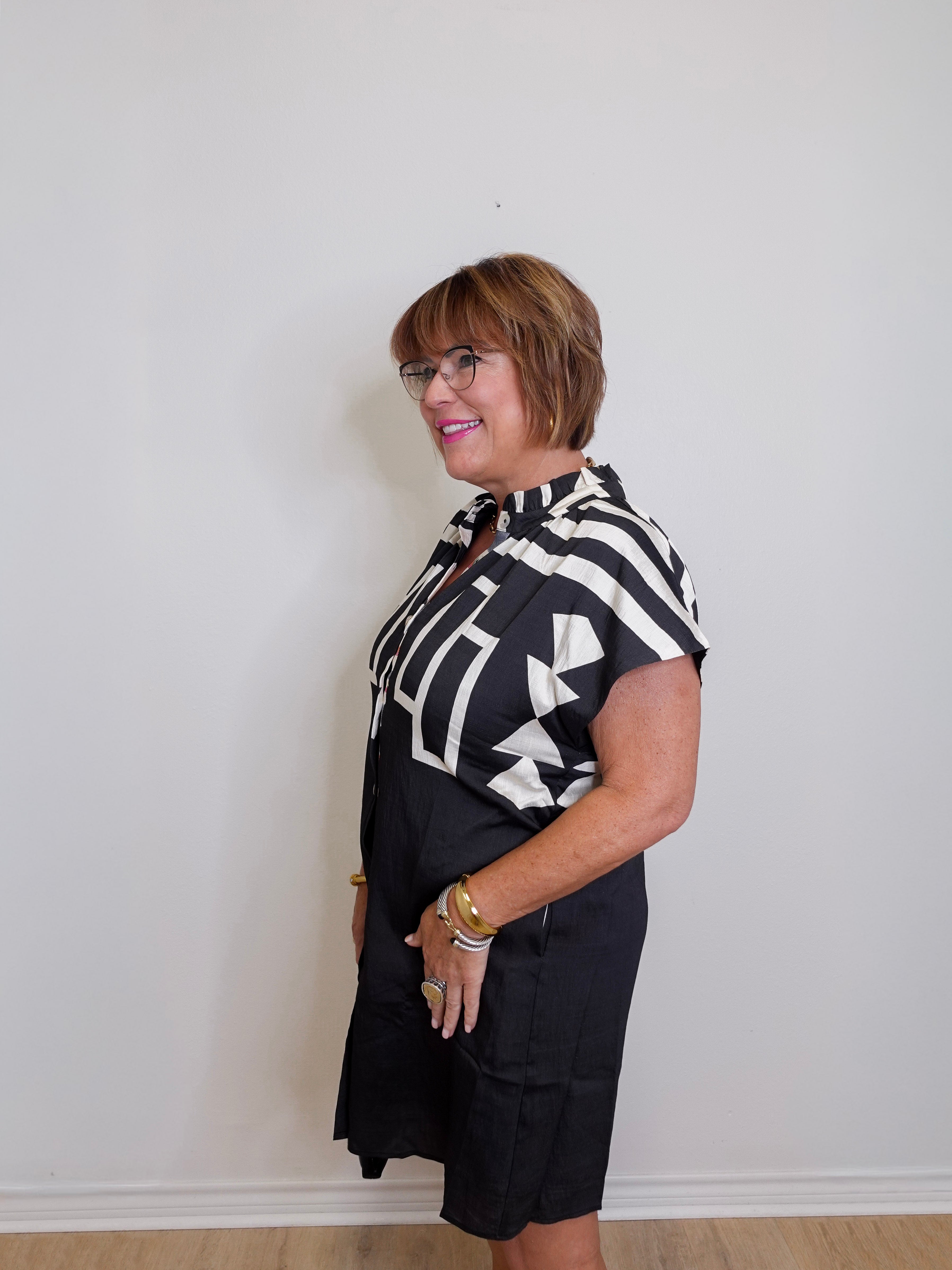 Woman wearing a black and white patterned blouse and black shorts against a plain background