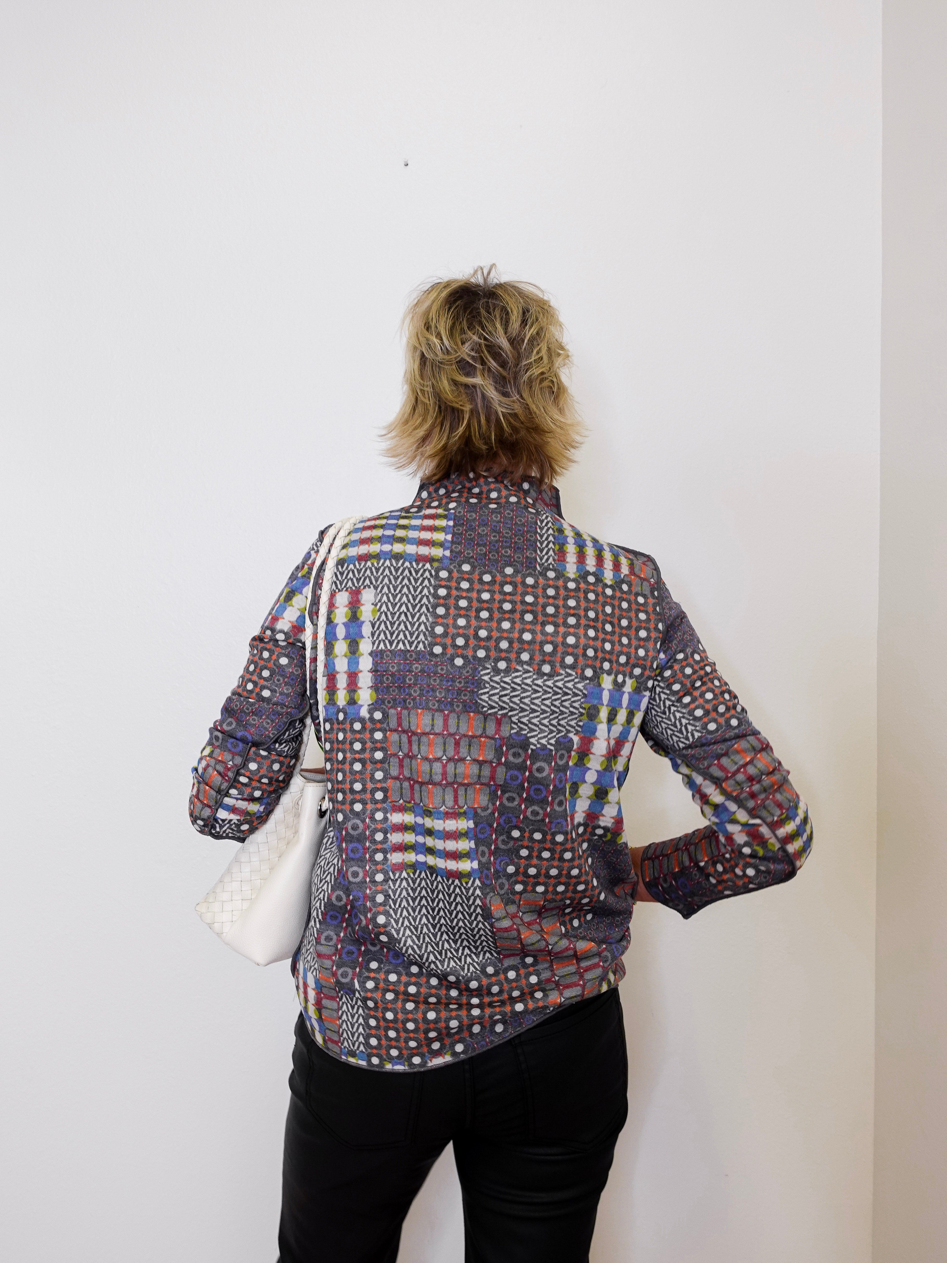 Person wearing a patterned shirt against a white wall