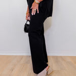 Person wearing a black outfit with wide-leg pants and open-toe shoes on a light wood floor.
