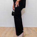 Person wearing a black outfit with wide-leg pants and open-toe shoes on a light wood floor.