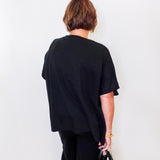 Person wearing a black outfit holding a black handbag against a white wall