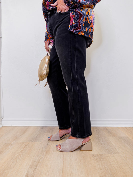 Person wearing a colorful patterned top, black pants, and beige sandals against a white wall.
