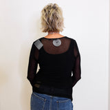 Person wearing a black long-sleeve top with sheer sleeves and blue jeans against a white background