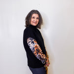 Woman wearing a black sweater with a leopard print sleeve against a white background