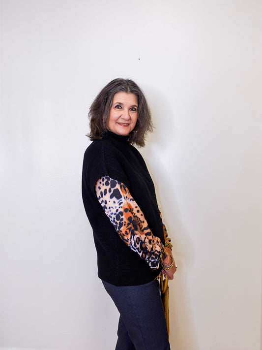 Woman wearing a black sweater with a leopard print sleeve against a white background
