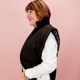 Woman wearing a black vest over a white shirt with a pink background