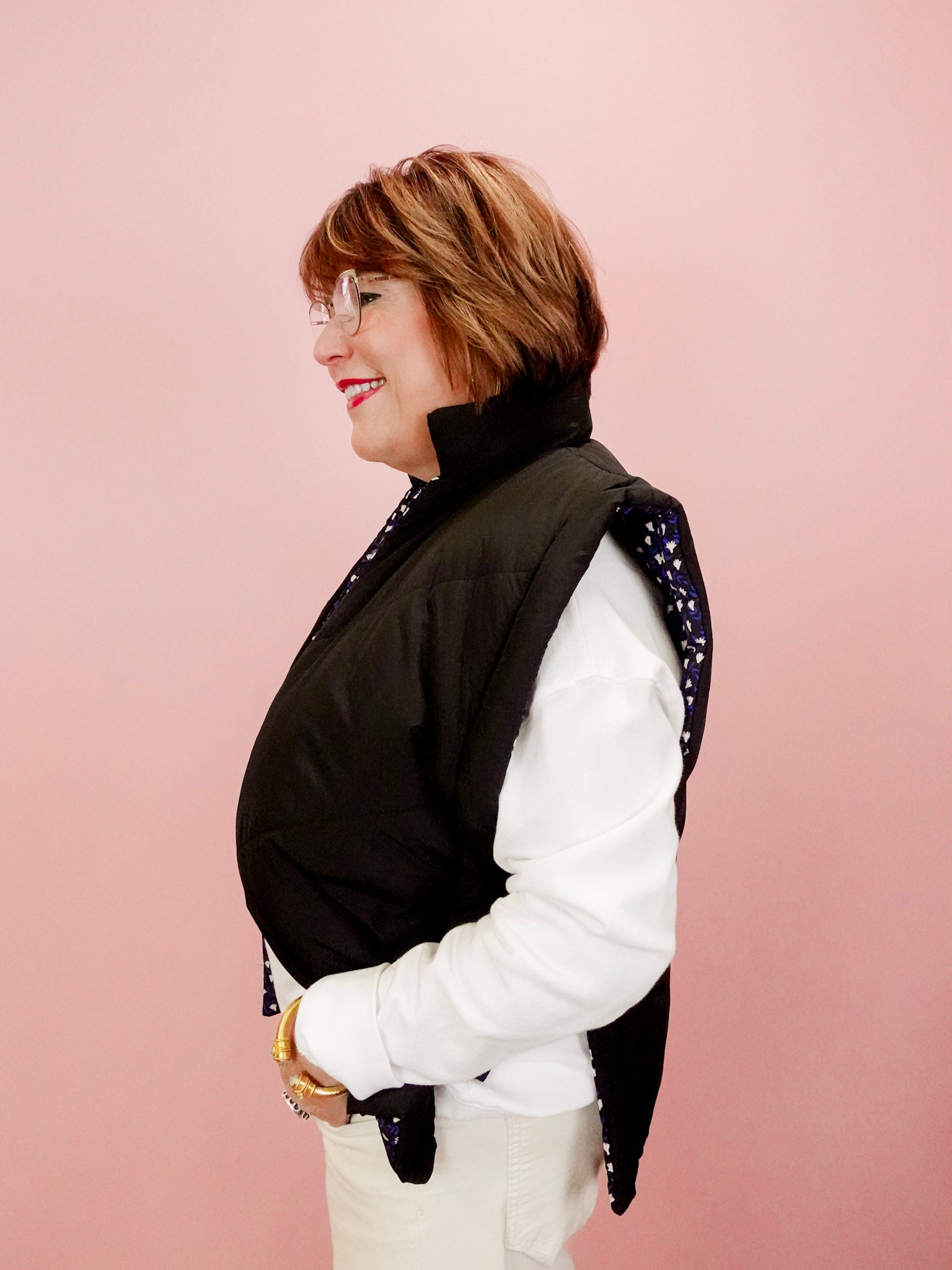 Woman wearing a black vest over a white shirt with a pink background