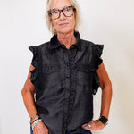 Woman wearing a black sleeveless shirt with ruffled details against a white background