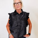 Woman wearing a black sleeveless shirt with ruffled details against a white background