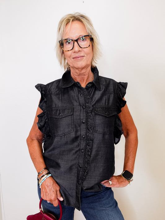 Woman wearing a black sleeveless shirt with ruffled details against a white background