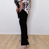 Person wearing a leopard print top and black pants on a light wooden floor.