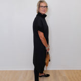 Person wearing a black outfit standing against a white wall.
