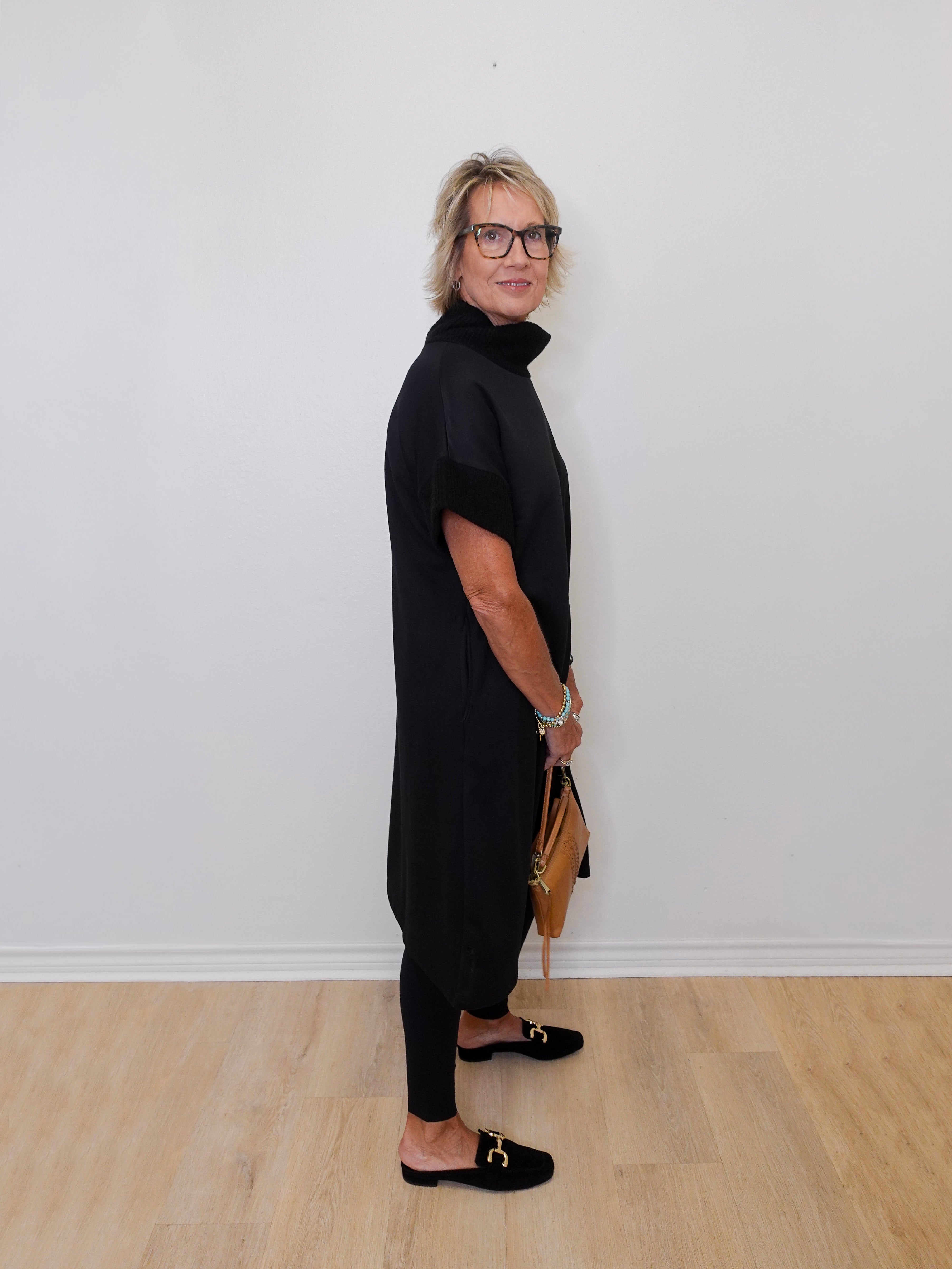 Person wearing a black outfit standing against a white wall.