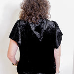 Person wearing a black velvet top with a plain background