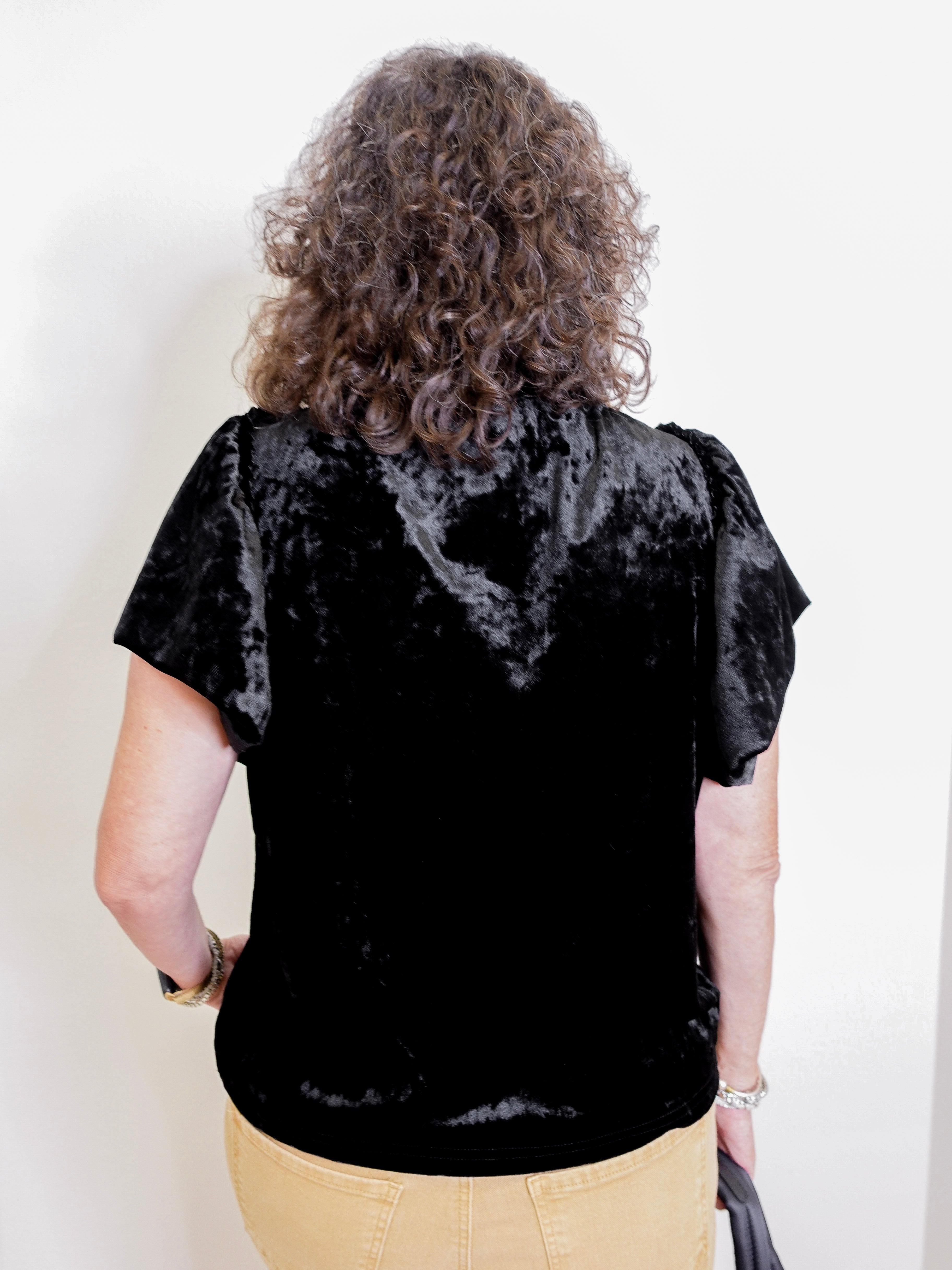 Person wearing a black velvet top with a plain background