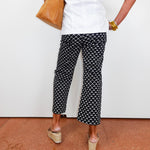 Person wearing black and white patterned pants with a white top and tan shoes on a red floor.