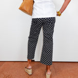 Person wearing black and white patterned pants with a white top and tan shoes on a red floor.