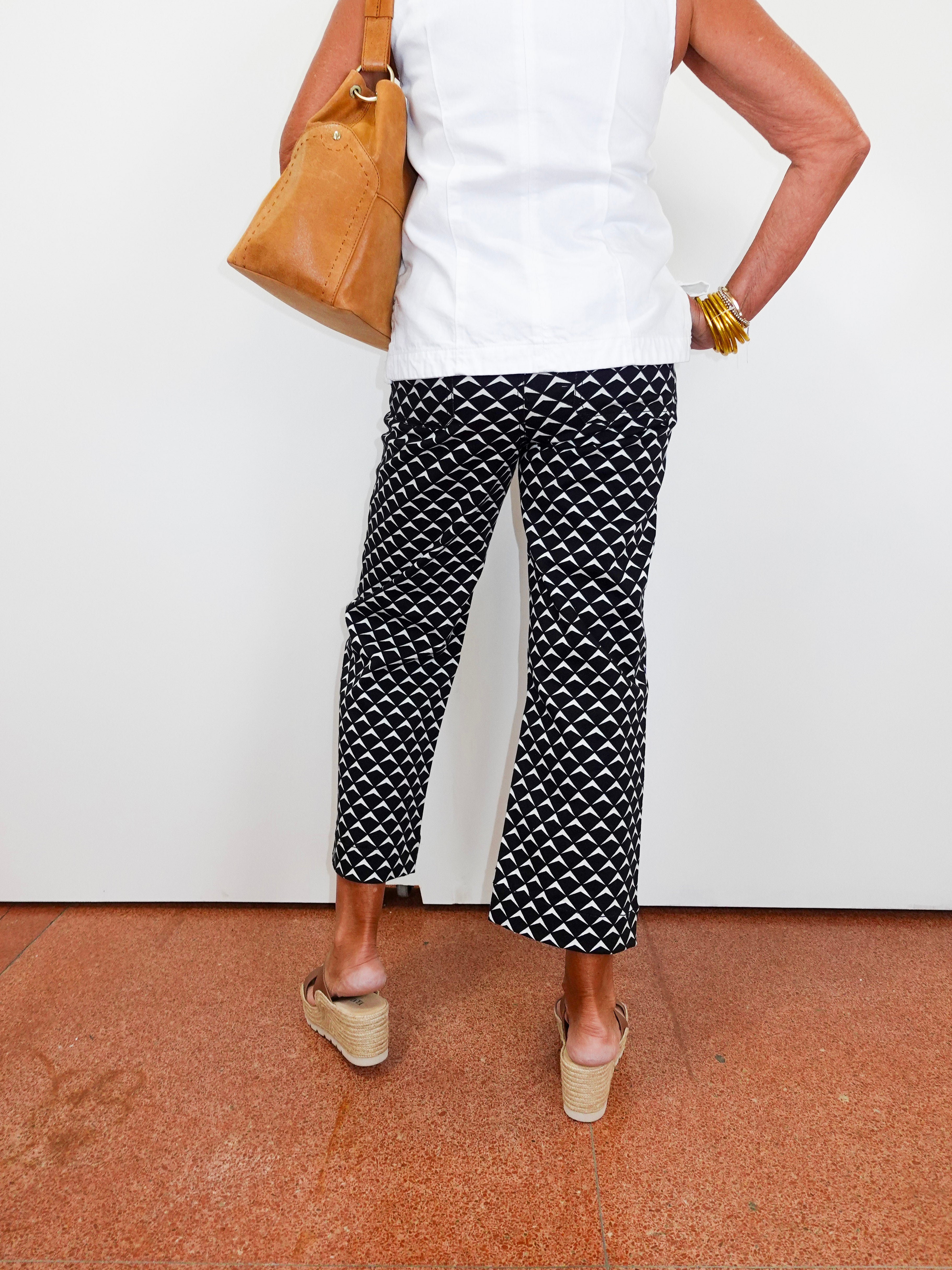 Person wearing black and white patterned pants with a white top and tan shoes on a red floor.