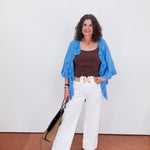 Woman wearing a blue jacket, brown top, white pants, and floral shoes against a white wall.