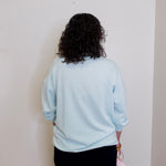 Person wearing a light blue sweatshirt against a plain wall