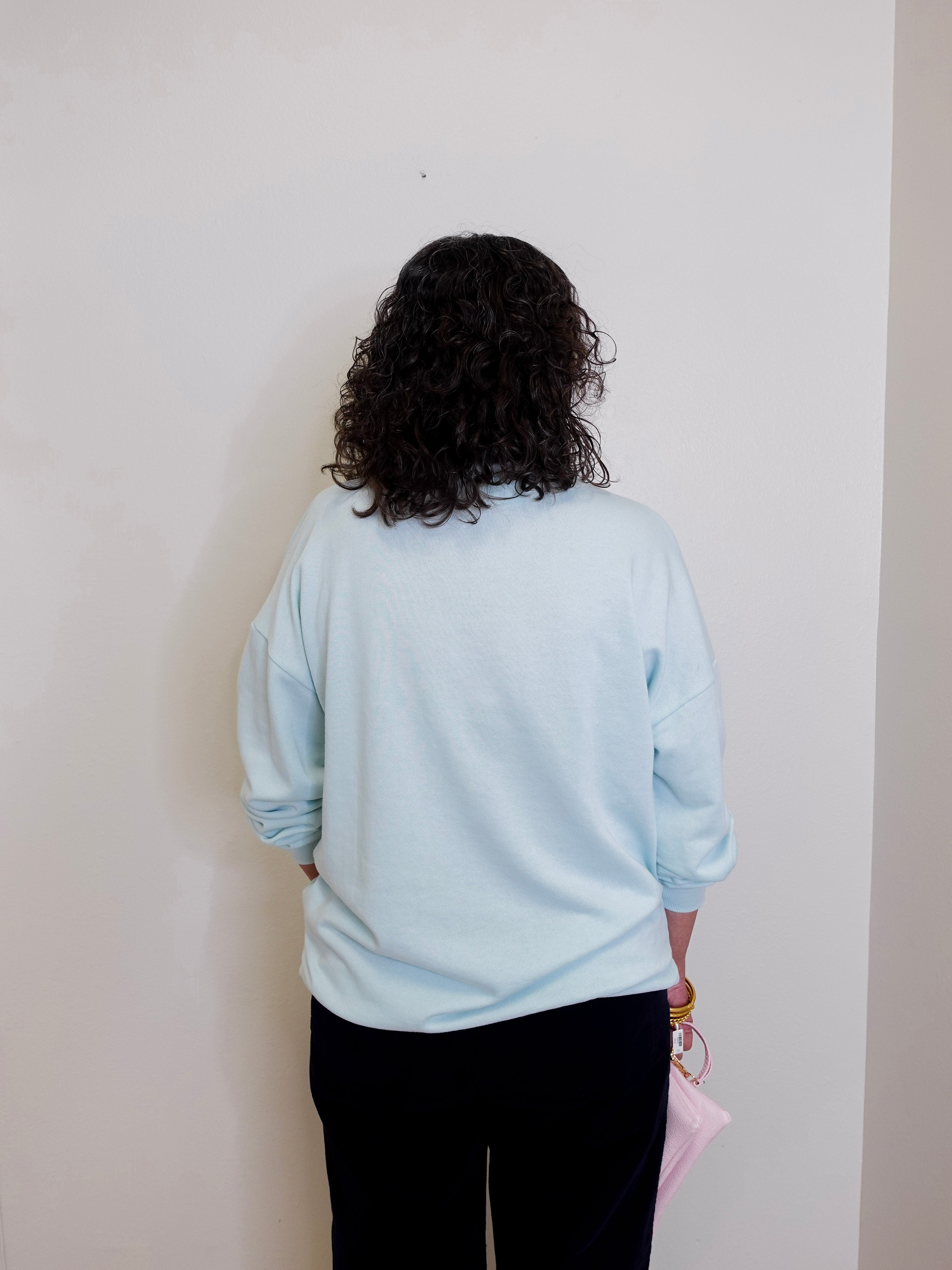 Person wearing a light blue sweatshirt against a plain wall