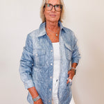 Woman wearing a blue denim jacket over a white shirt against a plain background