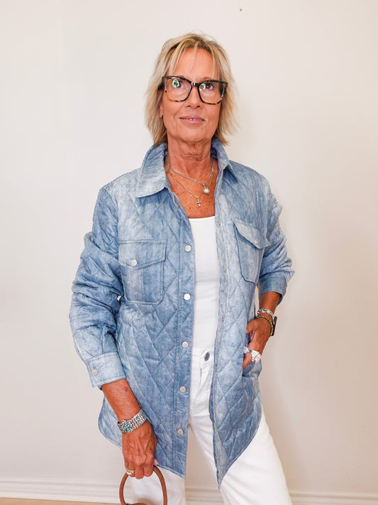 Woman wearing a blue denim jacket over a white shirt against a plain background
