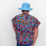 Person wearing a colorful patterned shirt and blue hat against a white background