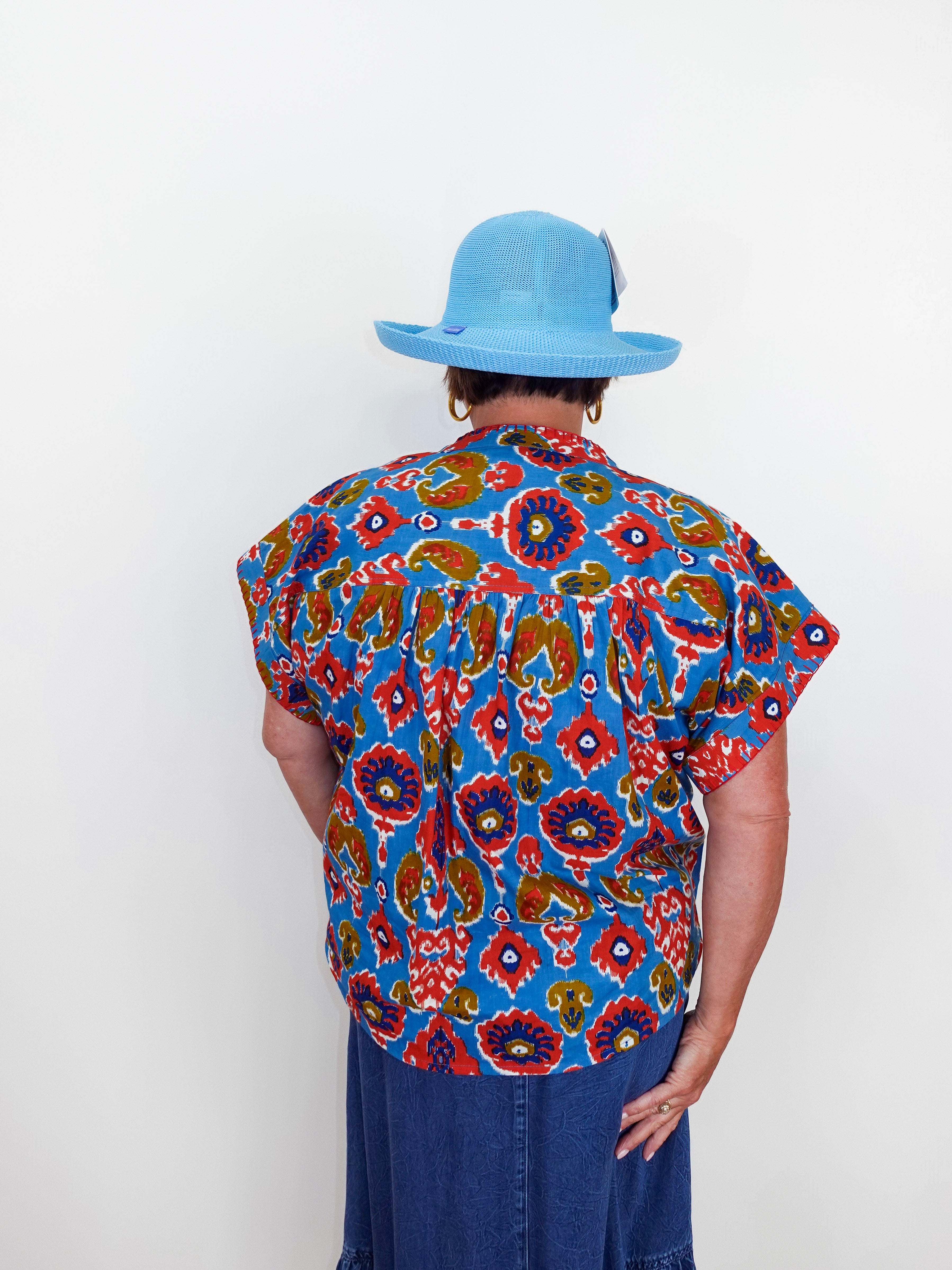 Person wearing a colorful patterned shirt and blue hat against a white background