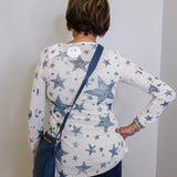 Person wearing a white long-sleeve shirt with blue star pattern, standing against a plain wall.