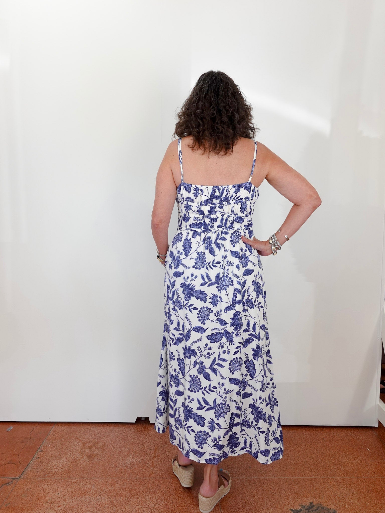 Woman wearing a blue floral dress against a white wall.
