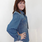 A woman with brown hair is wearing a blue denim long-sleeve button-up shirt and a white skirt with red polka dots, posing against a plain white background.