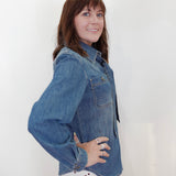 A woman with brown hair is wearing a blue denim long-sleeve button-up shirt and a white skirt with red polka dots, posing against a plain white background.