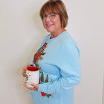Woman wearing a blue grandmas house holiday top against white background. 