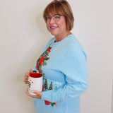 Woman wearing a blue grandmas house holiday top against white background. 