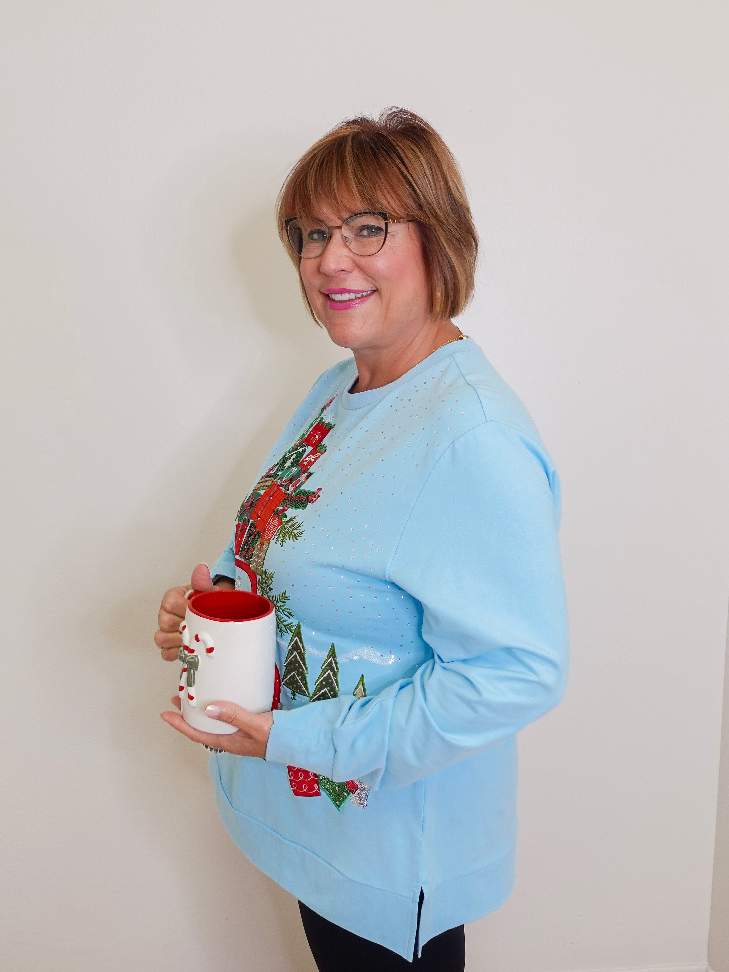 Woman wearing a blue grandmas house holiday top against white background. 