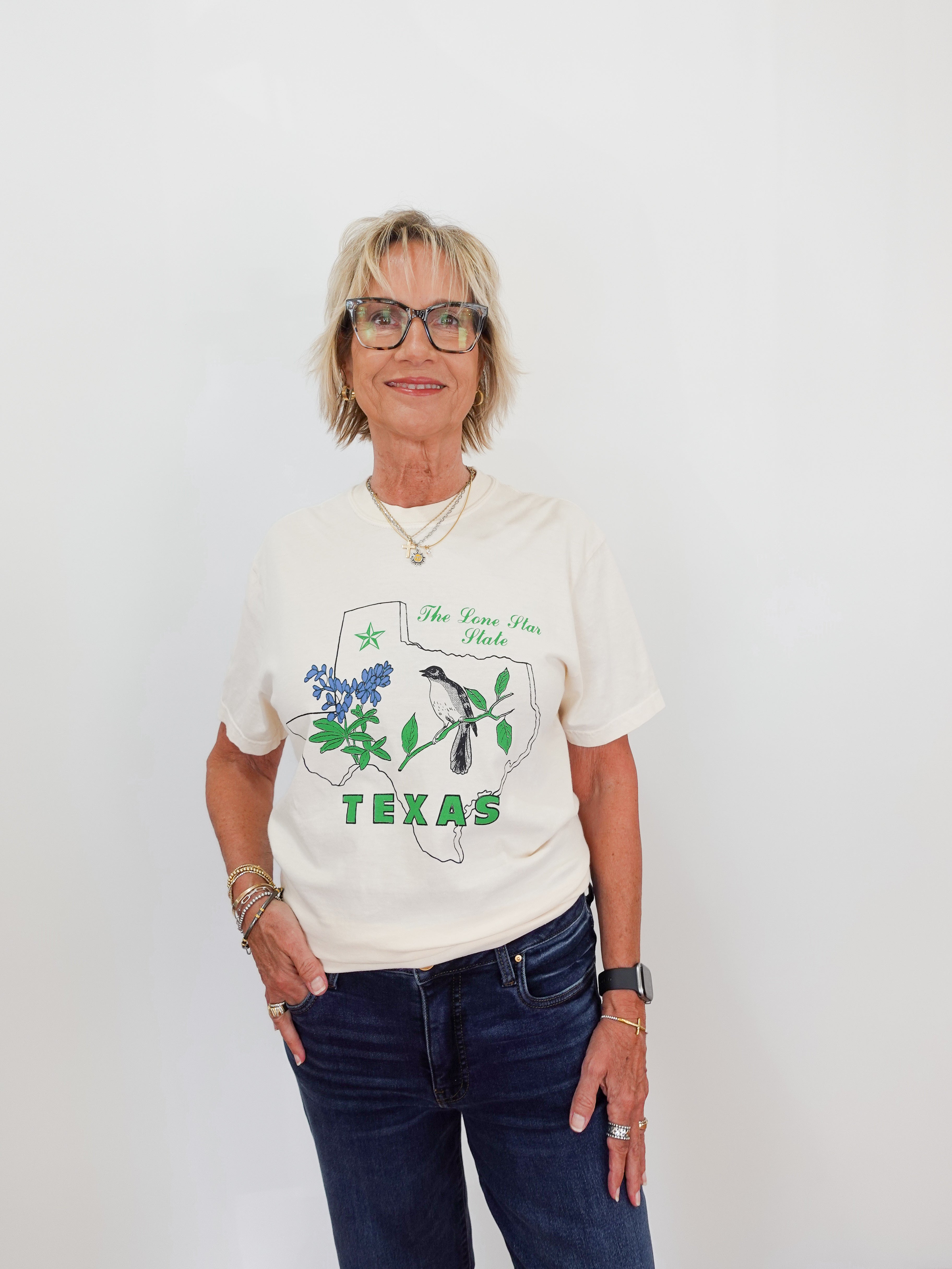 Woman wearing a white t-shirt with a graphic design and text, standing against a plain background.