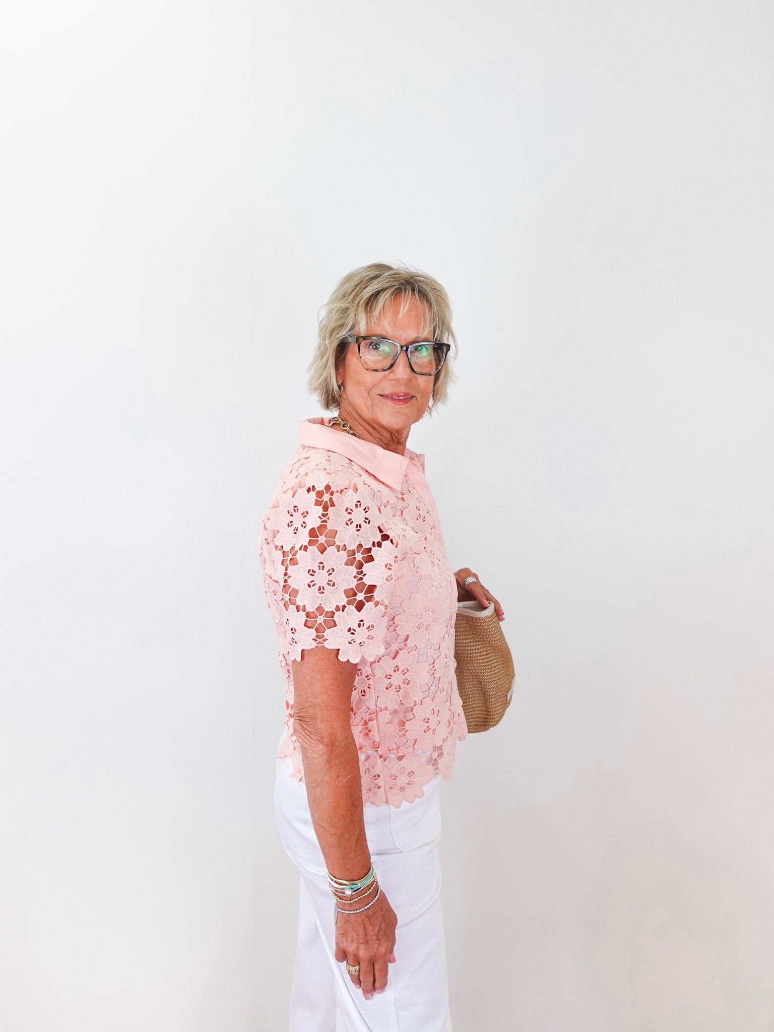 Woman wearing a pink floral top and white pants against a white background