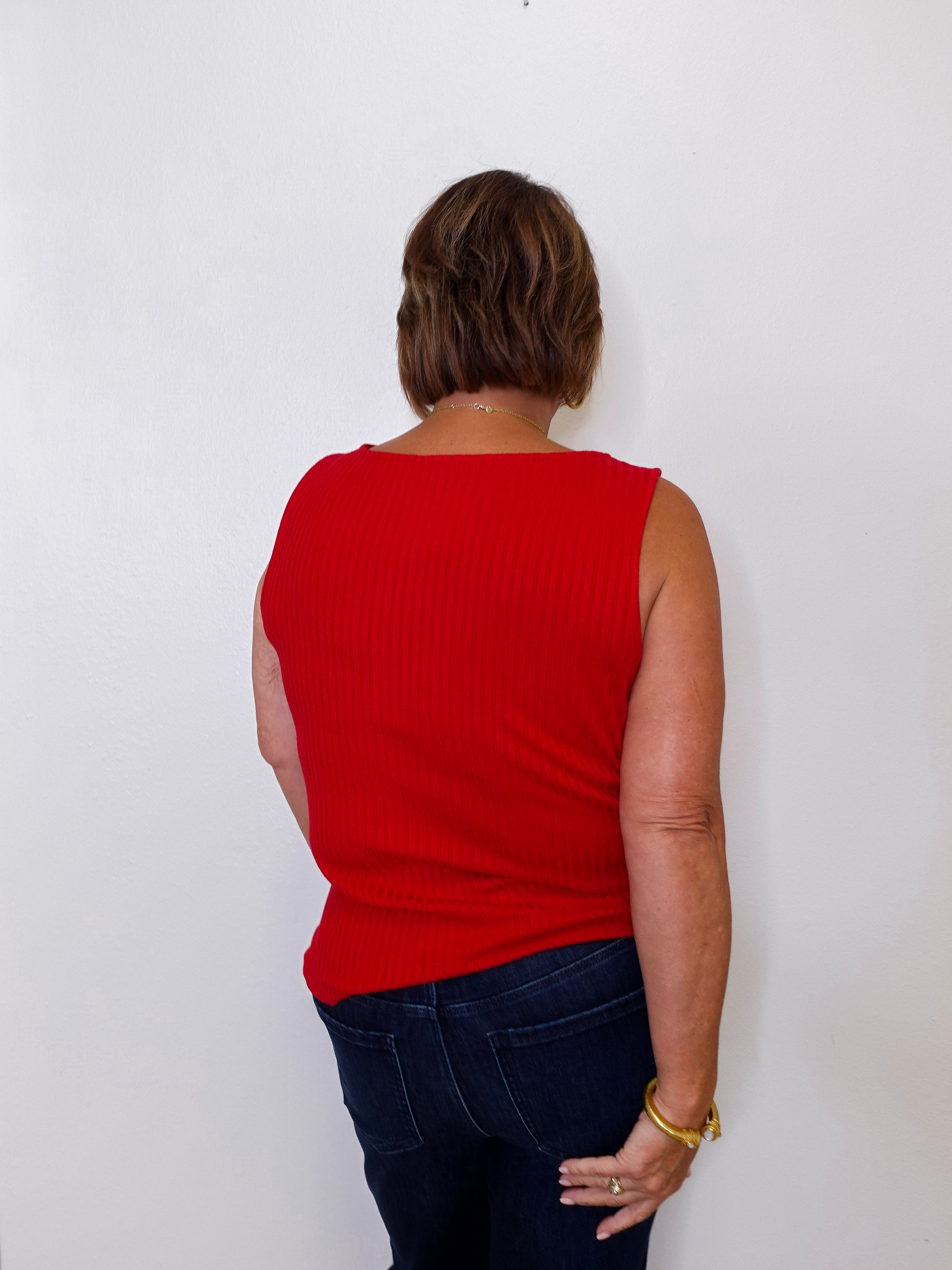 Person wearing a red sleeveless top and dark blue jeans against a white background