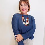 Woman wearing a blue sweater and colorful necklace against a white background