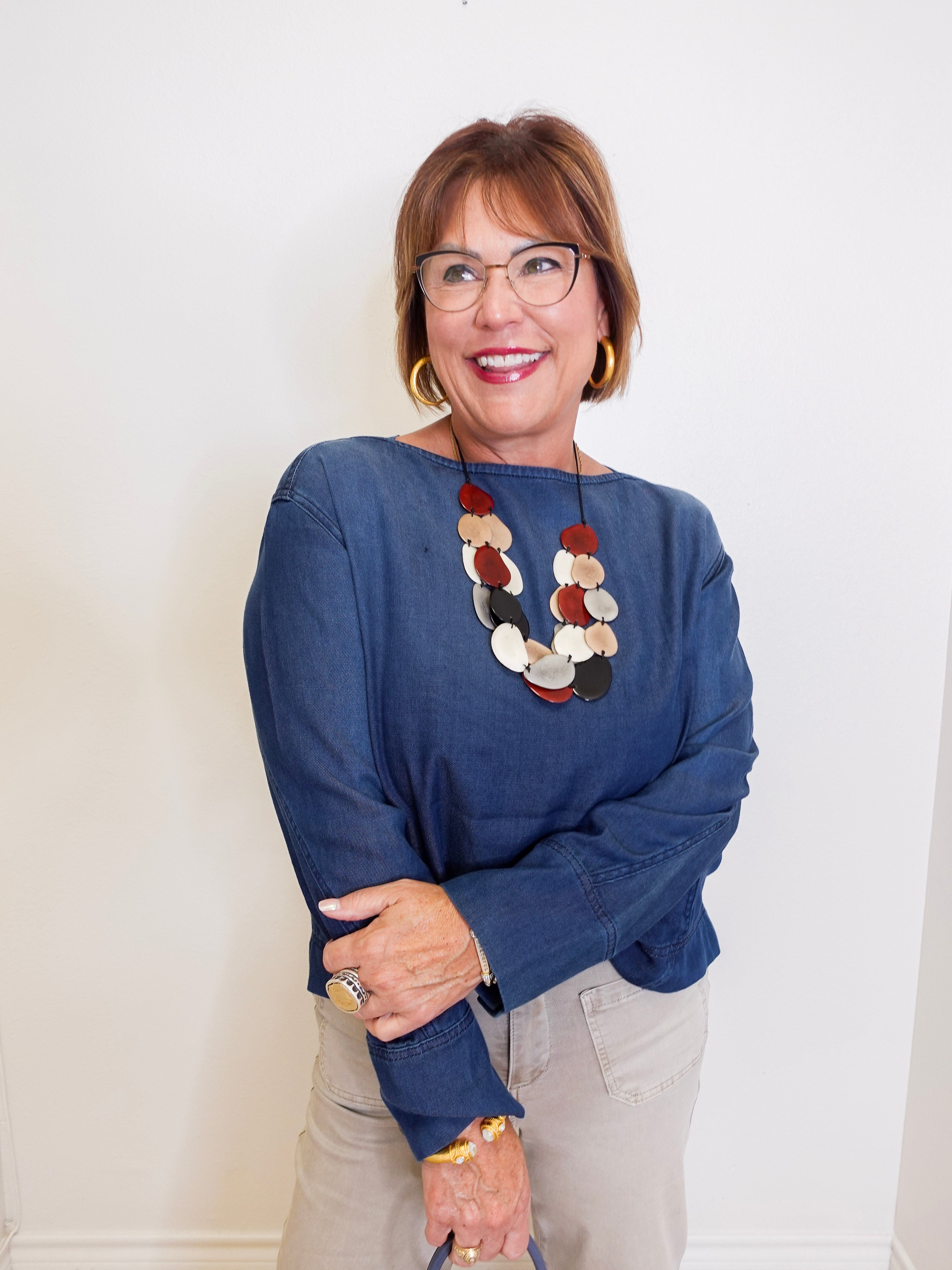 Woman wearing a blue sweater and colorful necklace against a white background