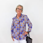 Woman wearing a colorful patterned shirt with white pants against a white background